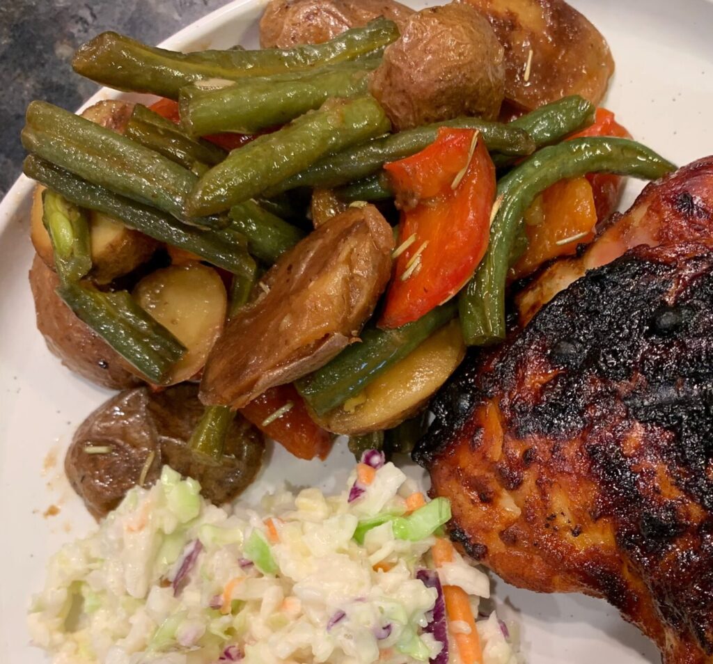 A plate of grilled barbecue chicken along with cole slaw and roasted veggie potato salad.