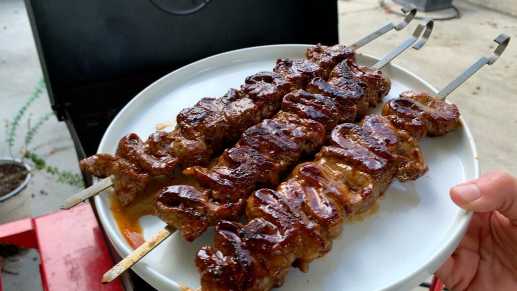 fresh off the grill, seared steak skewers sit atop a plate for service
