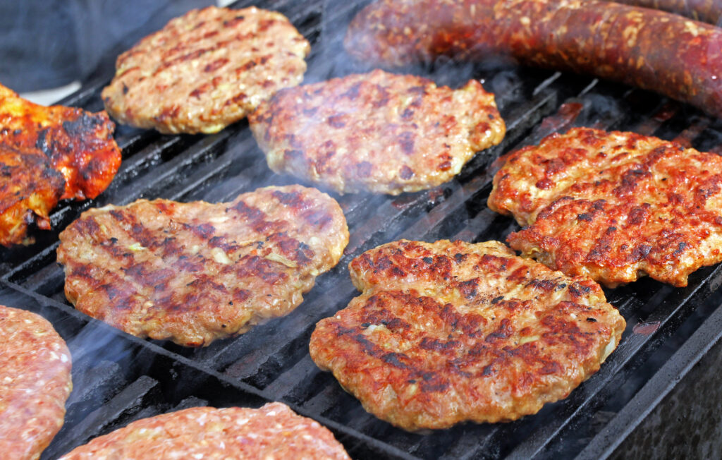 6 juicy burger patties on a charcoal grill.