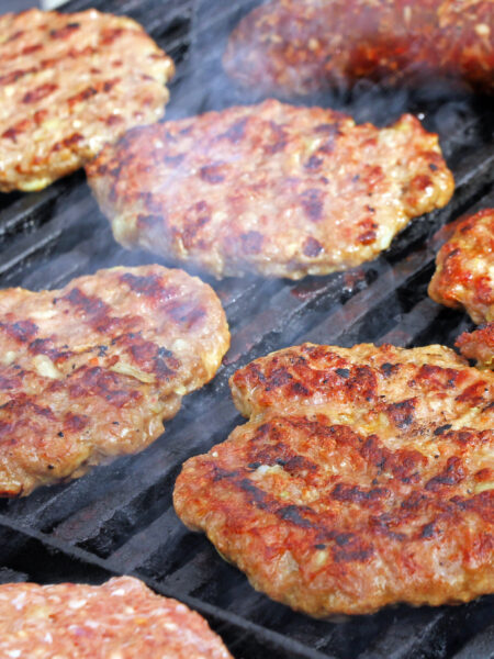 6 juicy burger patties on a charcoal grill.