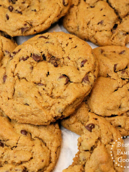 Several golden-brown peanut butter chocolate chip cookies piled on a white surface, with a watermark in the bottom right corner.