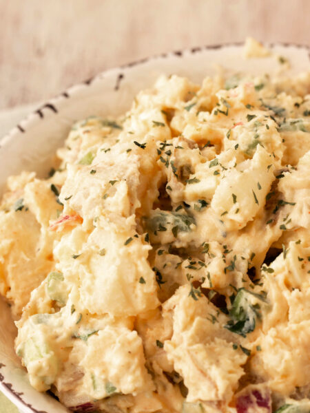 Creamy Southern potato salad with chunks of potato, chopped egg, relish, and parsley garnish in a rustic white bowl.