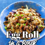 A blue ceramic bowl filled with an "Egg Roll in a Bowl" stir-fry consisting of browned ground meat, shredded cabbage, carrots, and sliced green onions.